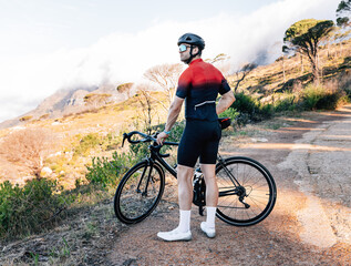 Back view of a professional road bike rider in fitness attire relaxing while standing on a roadside