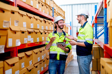 Two professional warehouse worker men discuss about work and stay between shelves with product in workplace and they look happy.