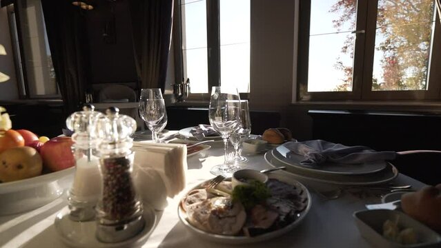 A table prepared in the afternoon in a restaurant near the window. Fully served with cutlery and food on a white tablecloth on a sunny day.