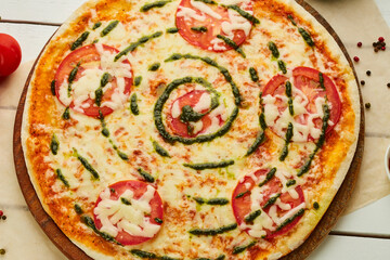 Freshly baked pizza Margarita with Tomatoes, Sauce Pesto and Mozzarella served on wooden background with sauces and herbs. Food delivery concept. Restaurant menu. Top View