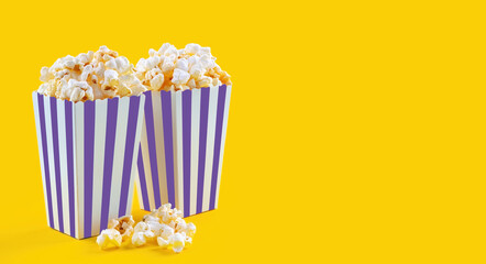 Two purple white striped carton buckets with tasty cheese popcorn, isolated on yellow background. Box with scattering of popcorn grains. Fast food, movies, cinema and entertainment concept.