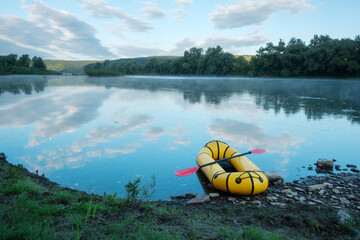 Yellow packraft rubber boat with red padle on a sunrise river. Packrafting. Active lifestile concept