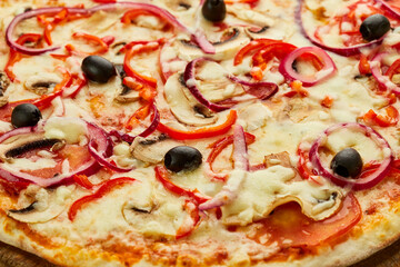 Freshly baked Vegetarian pizza with Tomatoes, mushrooms, red pepper, olives, onion and Mozzarella served on wooden background with sauces and herbs. Food delivery concept. Restaurant menu