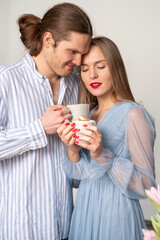 A mysterious man and a beautiful smiling young woman with red lips and nails. The two young people in light blue clothes drink coffee and enjoy each other's attention.