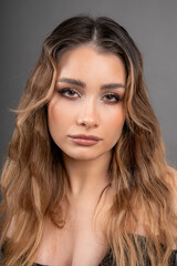 Fototapeta premium Portrait of face of young beautiful model with long well-groomed hair and professional makeup. Skin and hair care. 