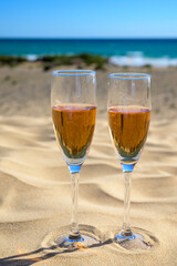 Two glasses of rose champagne or cava sparkling wine served on white sandy tropical beach with dunes and blue ocean, romantic vacation, winter sun on Fuerteventura, Canary, Spain