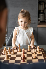 Little girl playing chess with her father at the table in home kitchen. The concept early childhood development and education. Family leisure, communication and recreation.