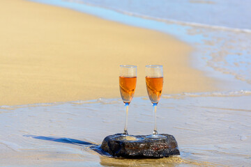 Two glasses of rose champagne or cava sparkling wine served on white sandy tropical beach and blue ocean water, romantic vacation, winter sun on Fuerteventura, Canary, Spain