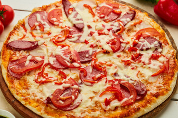 Freshly baked pizza with smoked sausages, red pepper and tomatoes served on wooden background with sauce and herbs. Food delivery concept. Restaurant menu