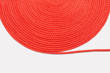 Red rope neatly twisted in a circle on a white background. Texture of red nylon rope close up. Roll of red rope. Free space for text. Neatly twisted textile rope