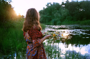 girl with flower wreath in hands near river, abstract natural green background. witchcraft ritual...