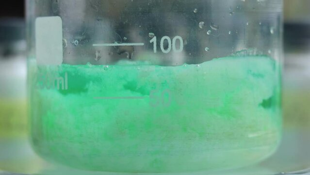 The chemical process of the formation of a large amount of sediment - an inorganic substance of nickel silicate of a beautiful green color in a beaker.
