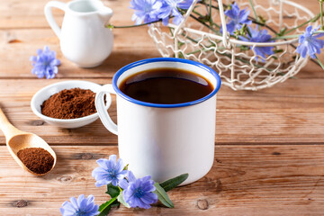 Drink made of chicory roots in cup, blooming chicory plants and spoon with granulated chicory root powder on wooden table. Caffeine free alternative to coffee.