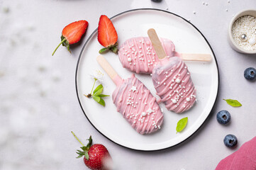 Cake pops ice cream on a stick in pink glaze on a plate with berries on a light background. Healthy homemade sweets. Party food.