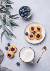 Cappuccino or latte with milk foam in a cup with  homemade berry cookies and blueberries on a light background with eucalyptus branches. Concept spring morning breakfast.
