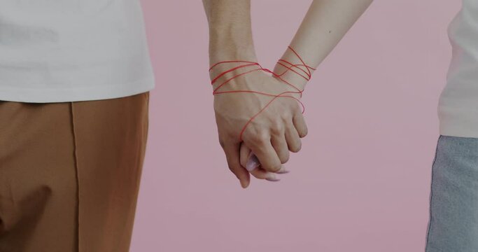 Male and female hands wrapped with red string touching holding against pink background. Romantic bond and loving relationship concept.
