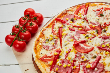 Freshly baked tasty pepperoni pizza with salami, mozzarella cheese, corn and pepper served on wooden background with tomatoes, sauce and herbs. Food delivery concept. Restaurant menu