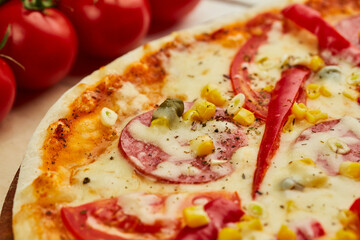 Freshly baked tasty pepperoni pizza with salami, mozzarella cheese, corn and pepper served on wooden background with tomatoes, sauce and herbs. Food delivery concept. Restaurant menu