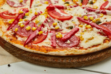 Freshly baked tasty pepperoni pizza with salami, mozzarella cheese, corn and pepper served on wooden background with tomatoes, sauce and herbs. Food delivery concept. Restaurant menu