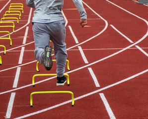 Rear view of runner running over mini hurdles on a track