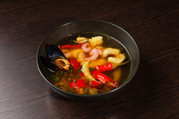 Appetizing looking seafood soup with mussels shrimp red peppers in a plate on a wooden table