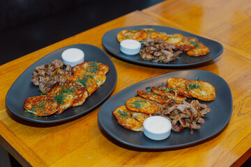 Plates with fried pancakes of potatoes fried meat with onions and sauce on a wooden table