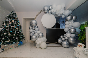 A round photo zone is made of white and silver balloons as well as a place for your inscriptions on a round plate. overall plan. Christmas tree