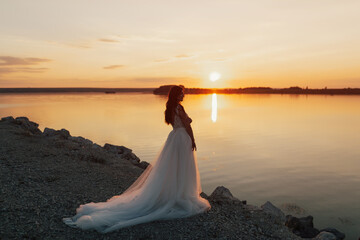 Bride in white long dress enjoy sunset at sea. Evening ceremony. Wedding ceremony seashore.