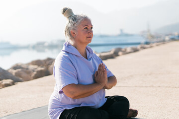 Fototapeta na wymiar Mindful senior woman with dreadlocks meditating by the sea and beach - wellness and yoga practice