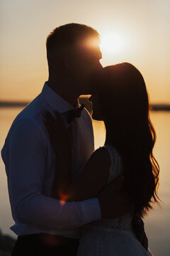 Silhouettes of couple on the background of the sunset and the sea. Man kissing his woman on the forehead. Close-up shot.