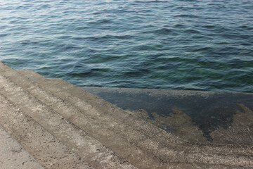 Obraz premium concrete embankment with stairs next to the blue sea in the sunshine on a spring and summer day