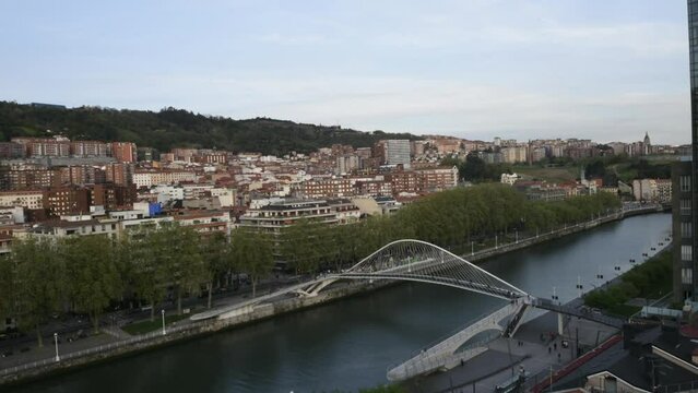High perspective timelapse of Zubizuri arch footbridge crossing the Nervion River in Bilbao, Spain - day to night