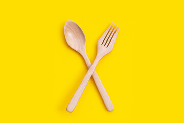 Wooden spoon and fork on yellow background.