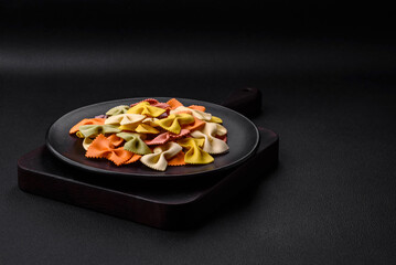 Raw farfalle pasta in different colors on a dark concrete background