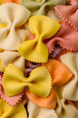 Raw farfalle pasta in different colors on a dark concrete background