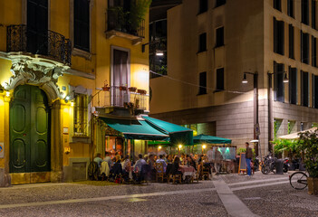 Old street with restaurant tables Milan, Italy. Night cityscape of Milan. Architecture and...