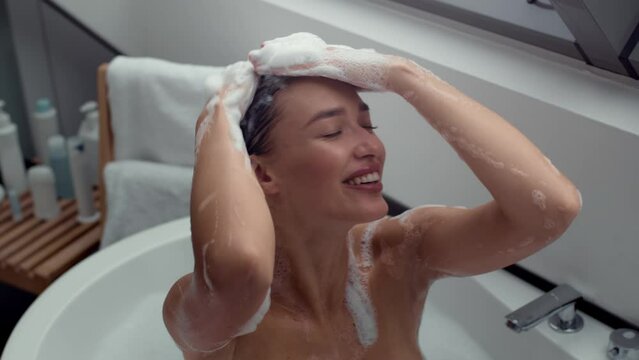 Top view portrait of young happy woman washing head sitting in hot bathtub, applying shampoo on long hair, tracking shot