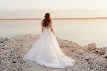 Fototapeta na wymiar Back view of beautiful bride in white long dress on the seashore. Sun horizon. 