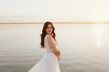 Fototapeta na wymiar Beautiful smiling young bride is posing at the sea view Wedding ceremony outdoors on the seashore. Summer sunset.