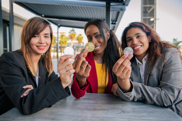 Three women hold three crypto coins in their hands during a meeting, females in the blockchain