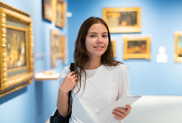 Portrait of a positive girl visitor with an information booklet attending an exhibition of...