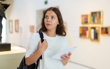 Portrait of an interested visitor girl with an information booklet, viewing an exhibit standing in an art gallery