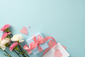 Mother's Day celebration concept. Top view flat lay photo of gift boxes with pink ribbons, carnation flowers, and pink paper hearts on pastel blue background with empty space for text or advert