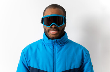 Close-up of a dark-skinned snowboarder wearing a blue padded jacket and goggles on a white background. Weekend Hobby Relaxation Hobby and winter extreme sports concept.