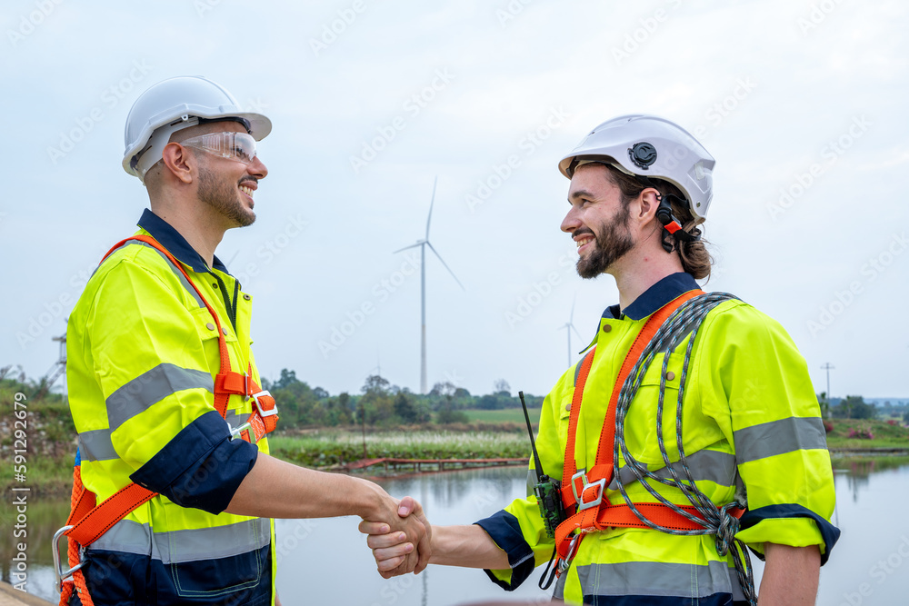 Poster engineers handshake after inspection work in wind turbine power generator station.