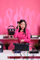 Asian artist with headphones having fun while playing techno music using professional mixer...