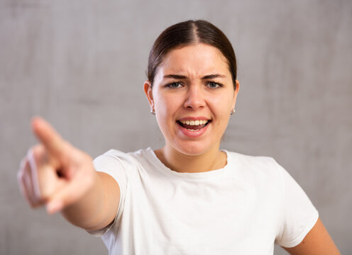 Portrait of embittered young woman shouting aggressively standing against gray shadeless background
