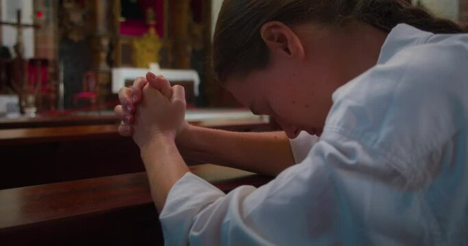 Christian woman prays on her knees in temple of the Lord. Close-up religious girl in church worshiping God.