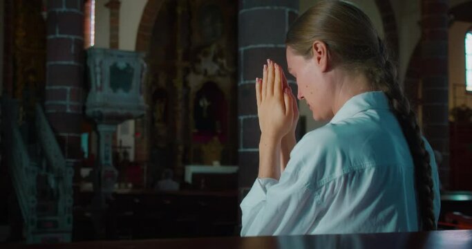 Woman bowed her head in prayer to God in a dark corner of church. Folded hands in prayer to Christ the Redeemer.