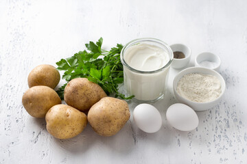 Ingredients for potato casserole: fresh potatoes, sour cream or heavy cream, eggs, flour, fresh parsley, salt, black pepper on a light blue background
